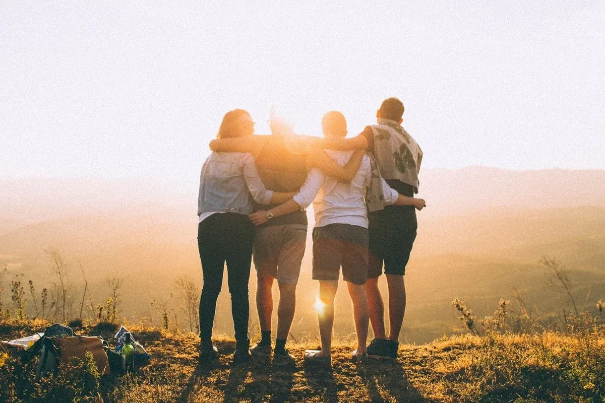 Cuatro amigos abrazados, de espaldas, mirando el atardecer desde una colina