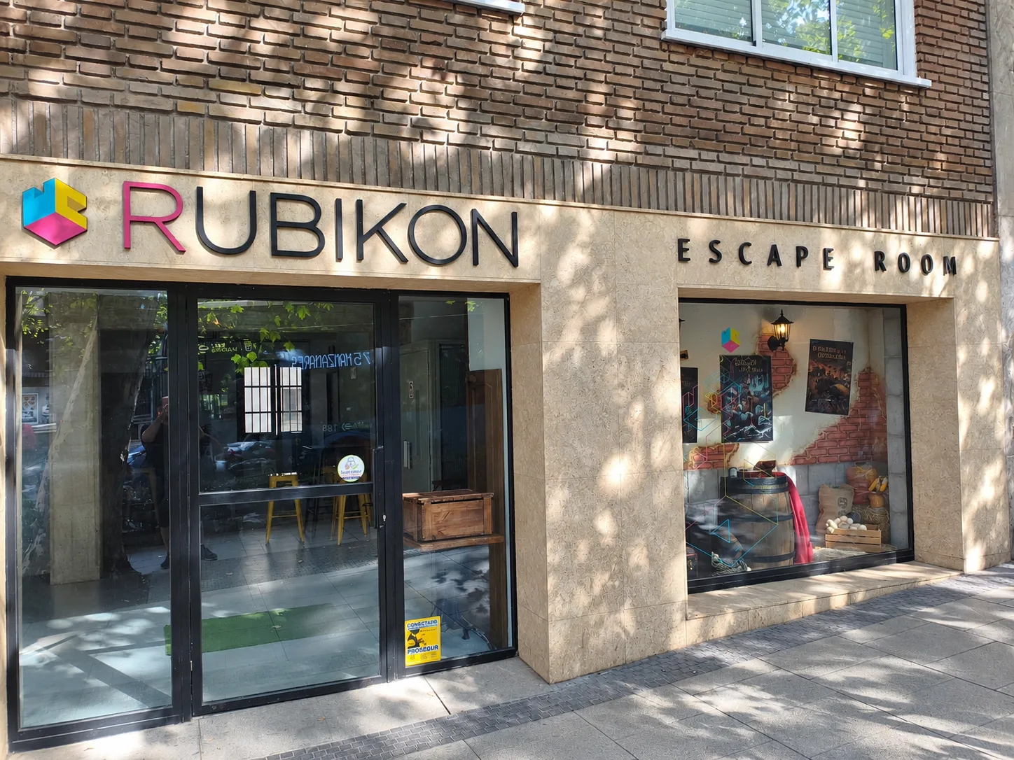 The front of Rubikon Escape Room: the sign with the three-colour cube on pale stone and, to its left, the glass entrance door