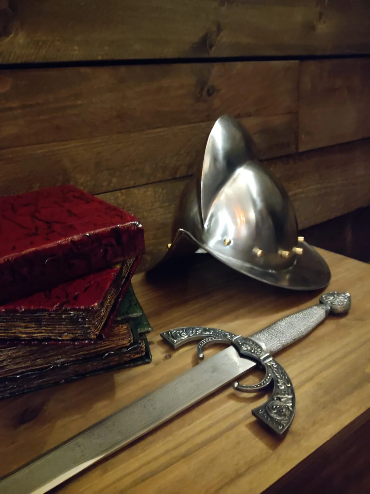 Worn red-bound books, a morion helmet and a sword with an engraved hilt