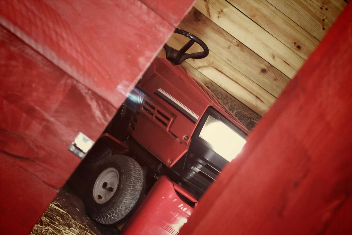 El tractor cortacésped rojo de la granja, visto por una rendija entre tablones